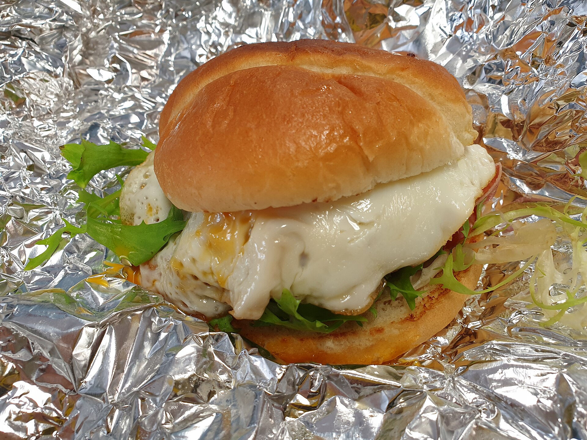 A cheeseburger with fried egg and greens