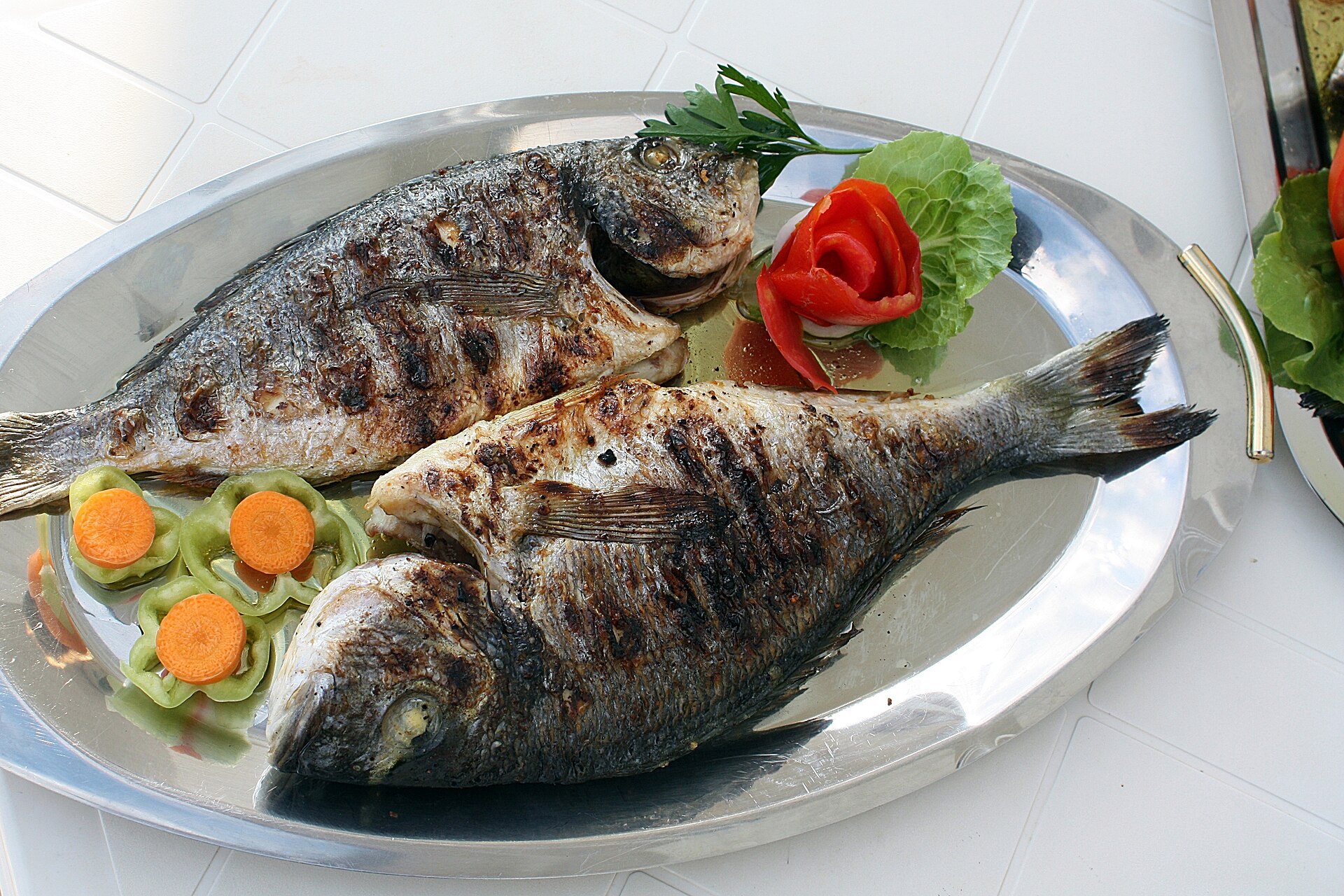 Two grilled fish served with vegetables