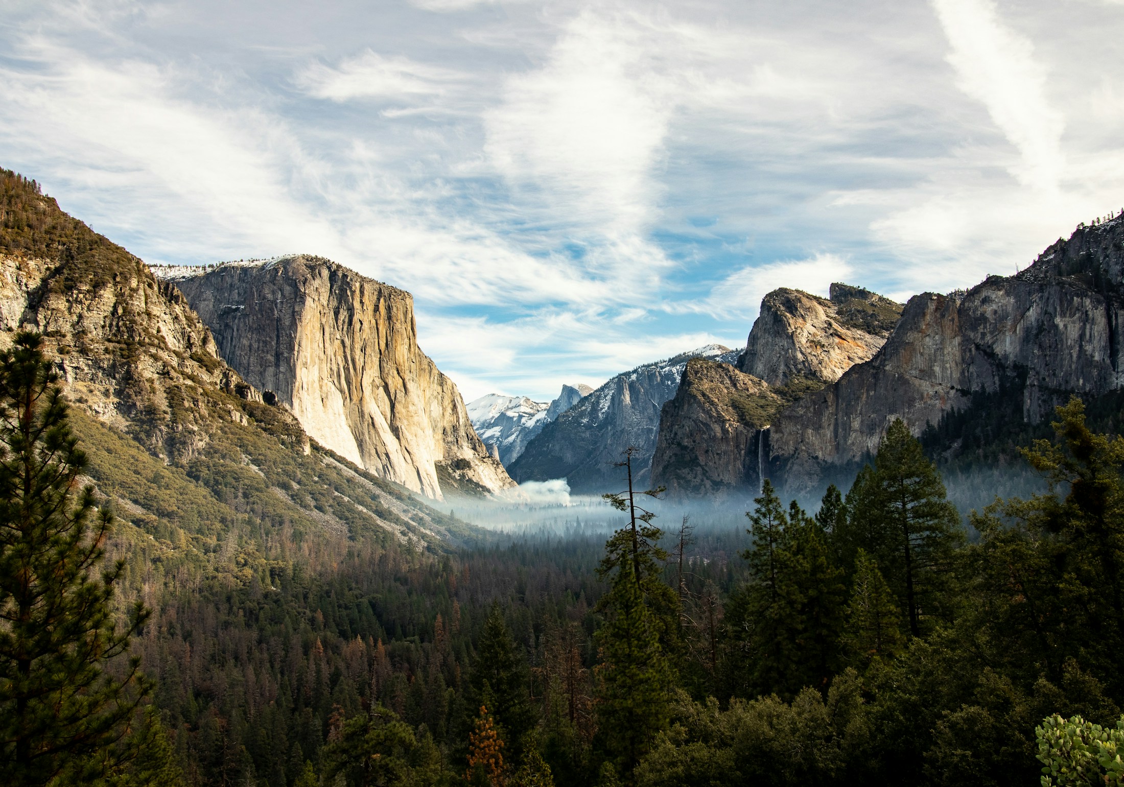 Granite cliffs, a forested valley and distant mountains in Yosemite National Park